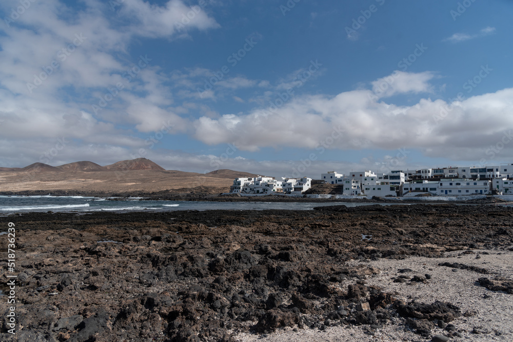 Panoramic view of Caleta de Caballo with the sea on calm and a light sand with rocks and caleta de Famara village at the back with the traditional White  House, nature of Lanzarote Canary islands