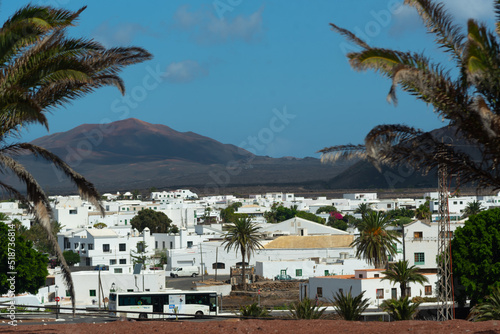 Panorámica del pueblo Yaiza en Lanzarote con sus pequeñas casas de color blanco, arquitectura típica de las Islas Canarias, con una gran montaña volcánica al fondo y rodeado por palmeras tropicales