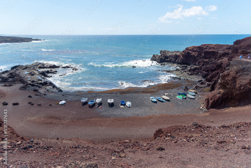 Panorámica de Playa del Golfo en Lanzarote., de arena negra con unas barcas pesqueras azules junto a unos acantilados de roca volcánica al lado del mar turquesa un día soleado de verano Islas Canaria