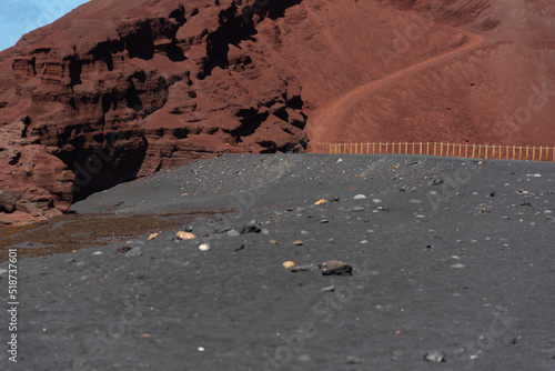 Gran montaña volcánica con un camino de tierra junto a una playa de arena negra en Lanzarote islas canarias, con una valla de madera separando la playa del la laguna de los clicos o charco verde. photo