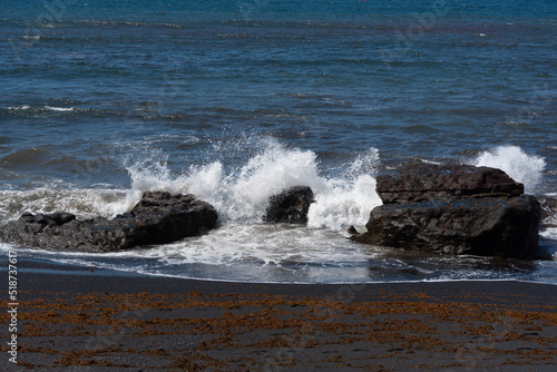 Olas rompiendo sobre rocas negras volcánicas en una playa de arena negra al lado de la Laguna de los Ciclos durante un día soleado de verano en Lanzarote, Islas Canarias.