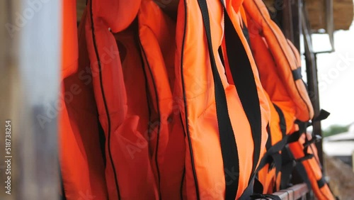 Orange life jackets in store by the sea. Many life jackets hang in a row on hangers. Protective safety clothing at rental boat store.
