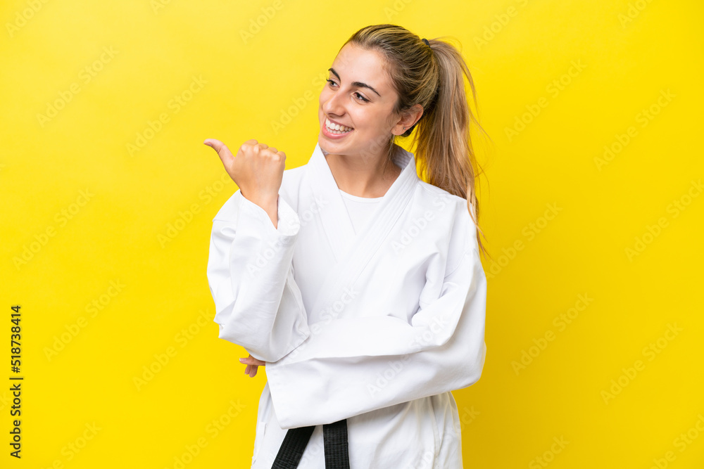 Young caucasian woman doing karate isolated on yellow background pointing to the side to present a product Young caucasian woman doing karate isolated on yellow background pointing to the side to present a product