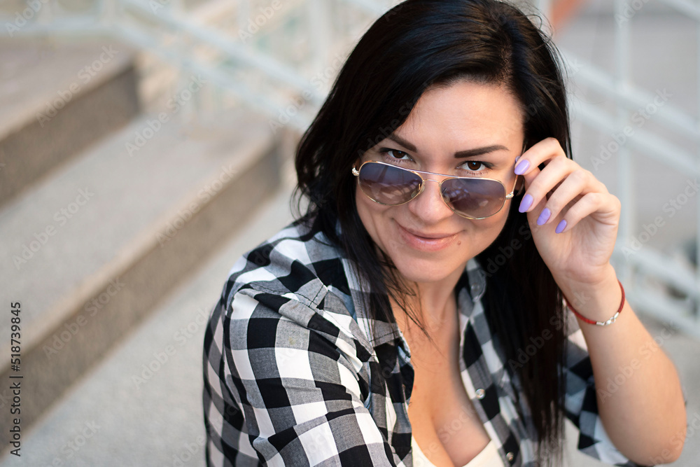 A girl of European appearance sits on the steps in the street with glasses. Close-up. A girl of European appearance sits on the steps in the street with glasses. Close-up.