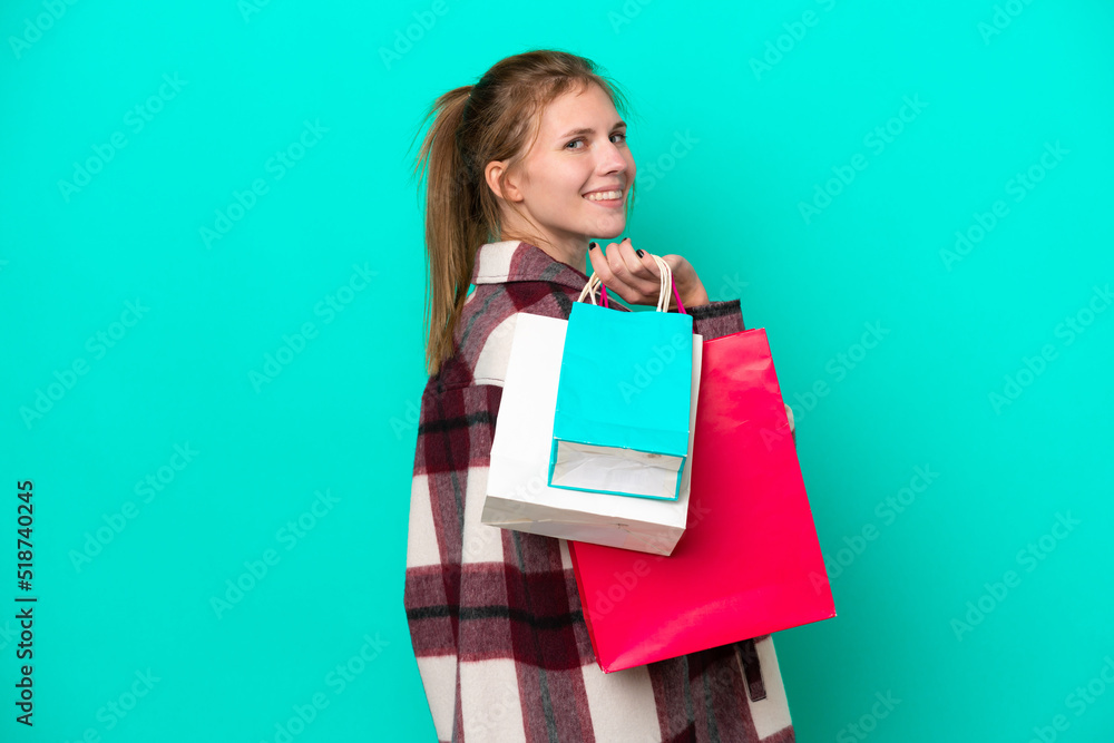 Young English woman isolated on blue background holding shopping bags and smiling Young English woman isolated on blue background holding shopping bags and smiling