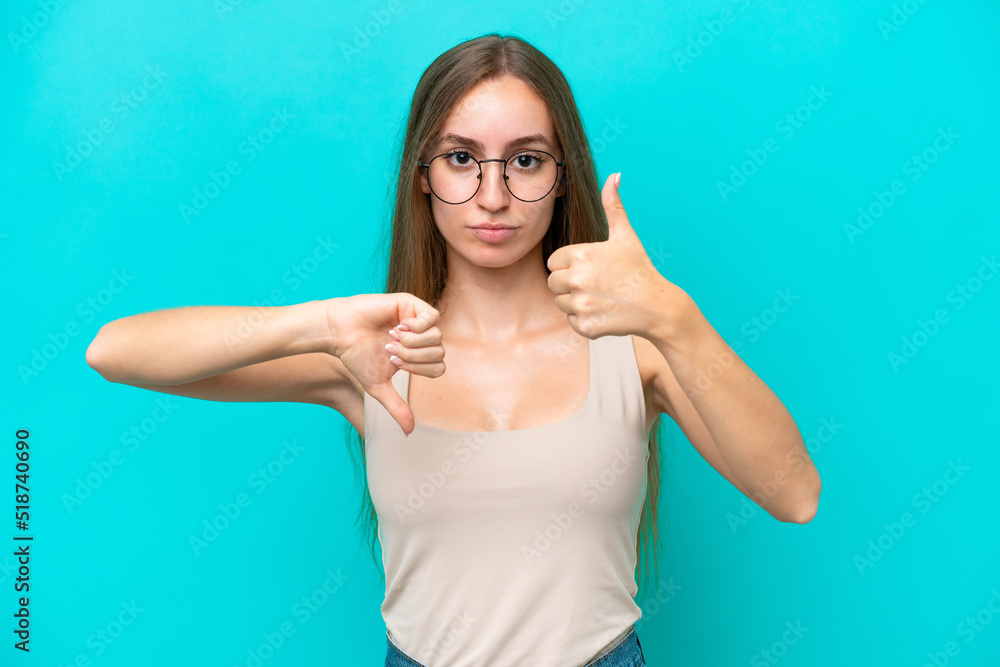 Fototapeta premium Young caucasian woman isolated on blue background making good-bad sign. Undecided between yes or not