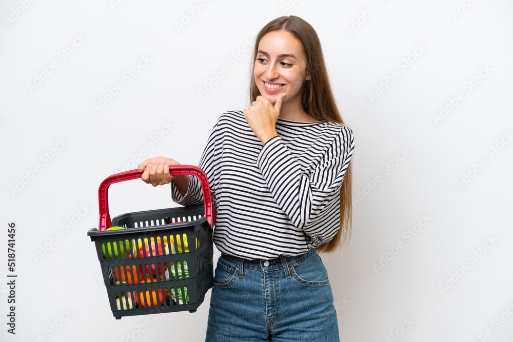 Young Rumanian woman holding a shopping basket full of food isolated on white background looking to the side and smiling Young Rumanian woman holding a shopping basket full of food isolated on white background looking to the side and smiling