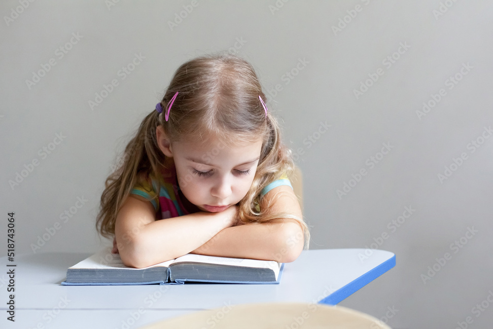 School child reading book on boring lesson. Tired pupil learning to read. Sad kid sitting at desk in classroom in elementary college. Primary student overworked. Education, back to school concept School child reading book on boring lesson. Tired pupil learning to read. Sad kid sitting at desk in classroom in elementary college. Primary student overworked. Education, back to school concept