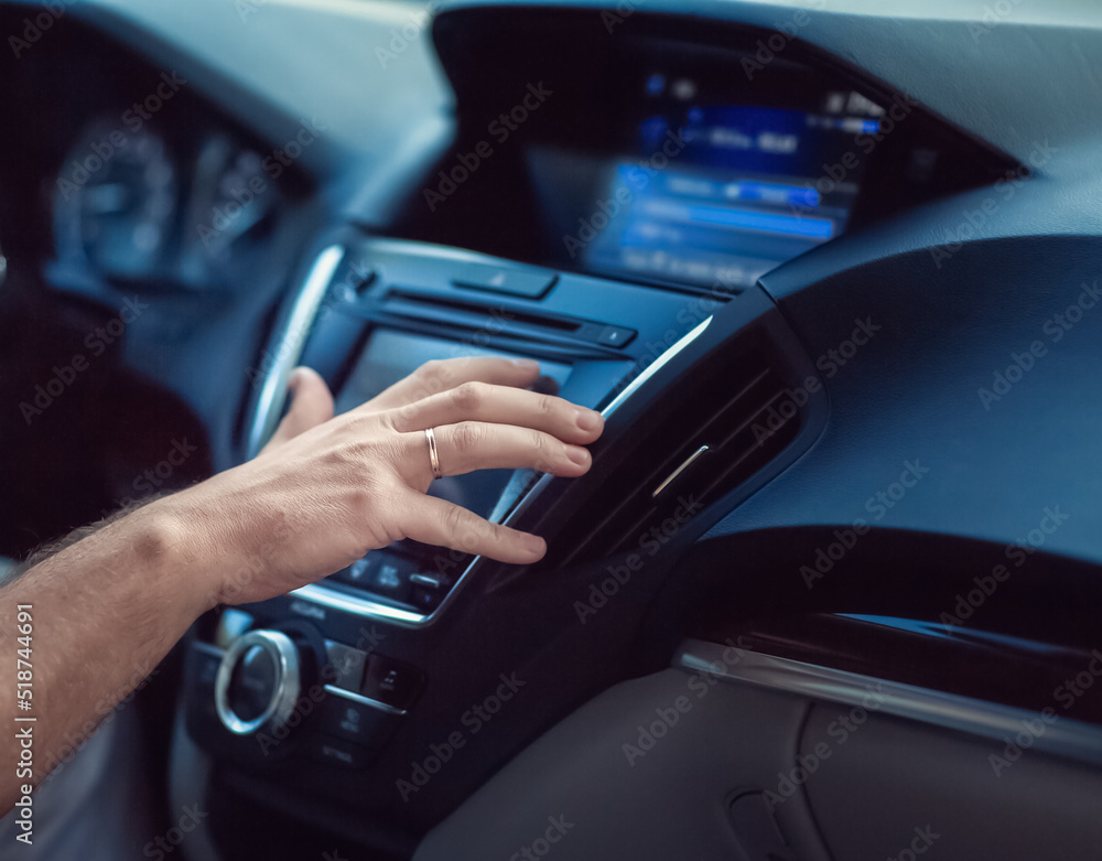 A man sits in a car and sets up music in the car. The photo shows a close-up of the hand. Ring on the finger. Expensive comfortable car.