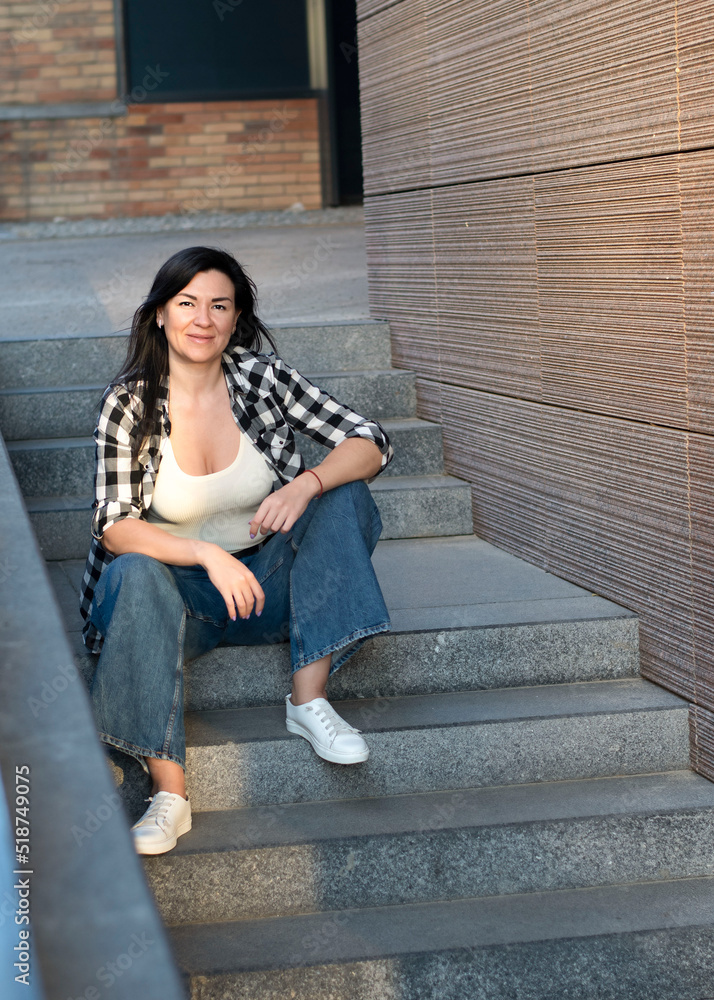 Young beautiful woman sits on the steps near the building on the street in summer. Sunset light.