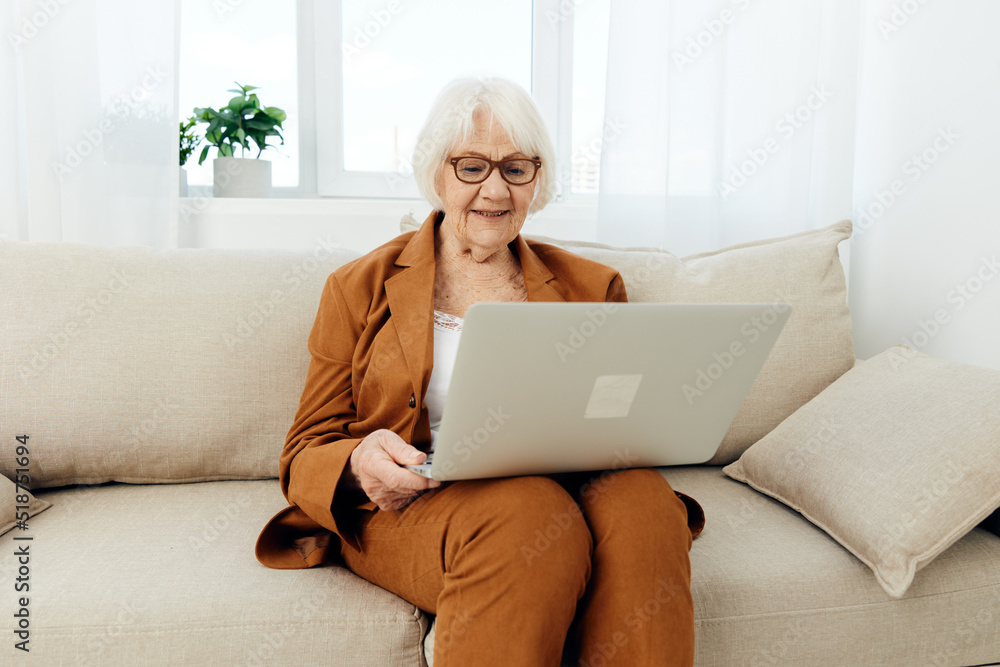 an experienced, elderly woman is sitting on a sofa in a brown suit, holding a video conference on a laptop, passing on her knowledge to a new generation an experienced, elderly woman is sitting on a sofa in a brown suit, holding a video conference on a laptop, passing on her knowledge to a new generation