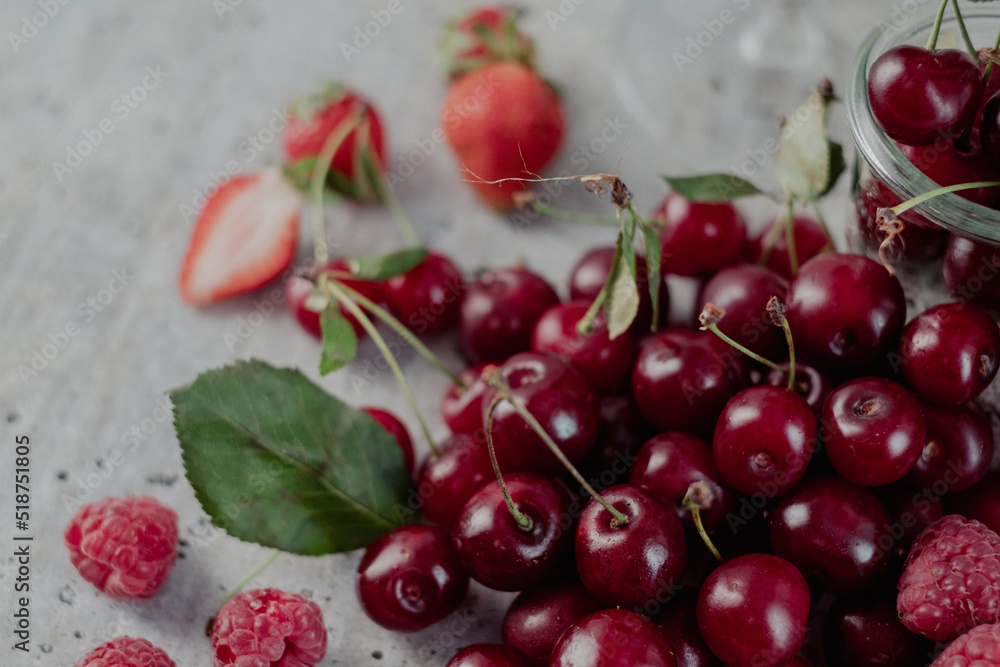 Appetizing, fresh, juicy, ripe cherry, strawberry and raspberry assortment on light gray background. Cherry leaf in the background. Appetizing, fresh, juicy, ripe cherry, strawberry and raspberry assortment on light gray background. Cherry leaf in the background.