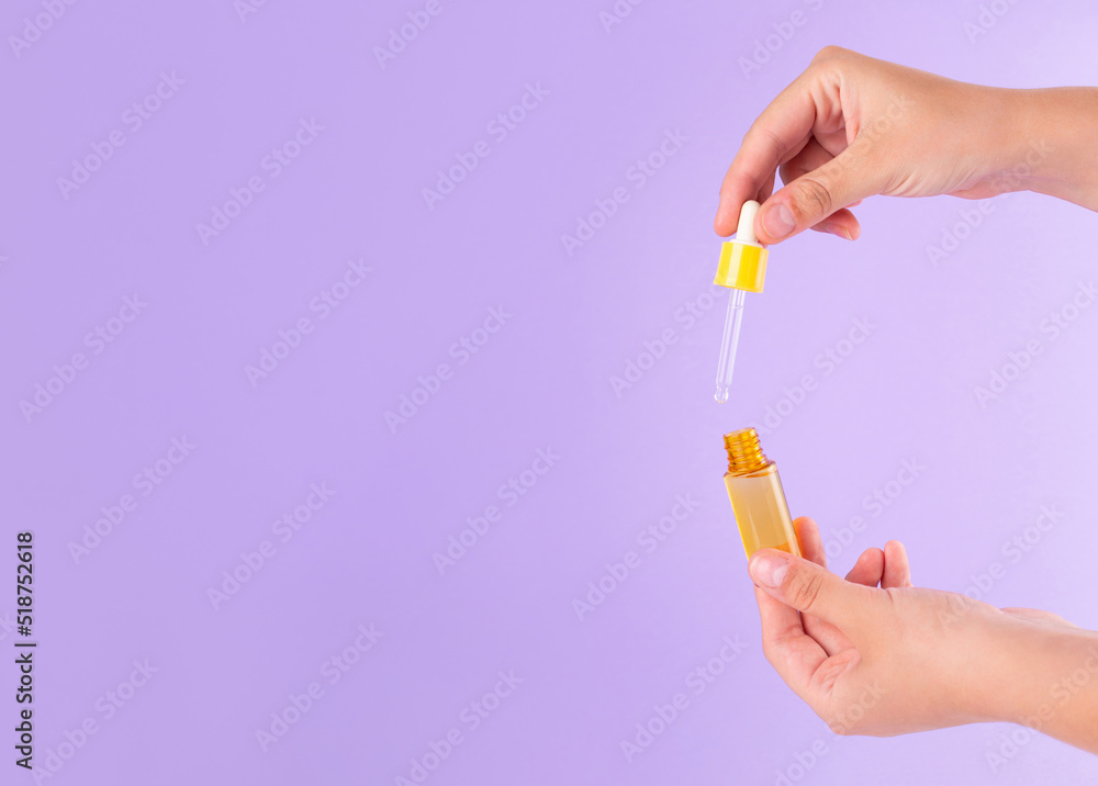 glass yellow bottle with pipette with essential oil in female hand on purple background top view. Aromatic cosmetic product for skin hair care Moisturizing beauty product with vitamin C close up glass yellow bottle with pipette with essential oil in female hand on purple background top view. Aromatic cosmetic product for skin hair care Moisturizing beauty product with vitamin C close up