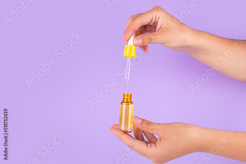 Serum bottle in female hands, top view. Yellow moisturizer for skin care. Nourishing essential oil in glass bottle with pipette. Liquid emulsion with hyaluronic acid. Beauty cosmetic spa product