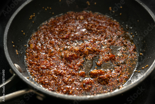 Cooking a spicy sauce with ginger, garlic, chili, tomato paste and sesame seeds in vegetable oil in a pan, selected focus,