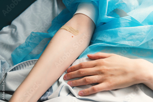 Close-up of a woman's hand with a band-aid on her arm. Patient lying on a hospital bed after surgery. 