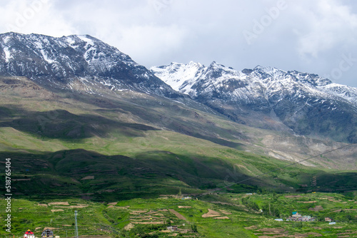 Vast landscape of snow capped mountains and lush green terrace farming.Small village houses can also be seen and beautiful sun shadow passing through mountains.Monsoon view of himalayan village india.
