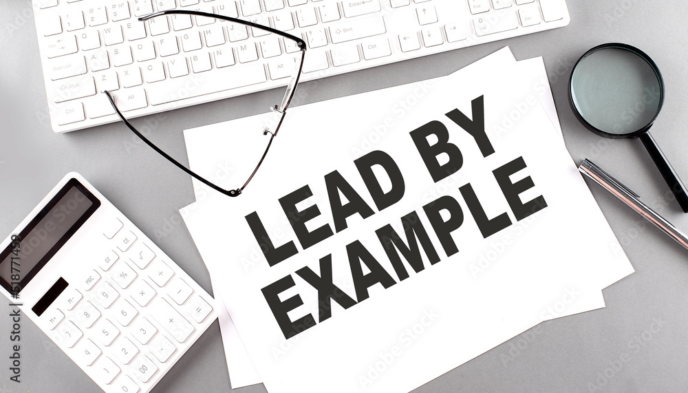 LEAD BY EXAMPLE text on paper with keyboard, calculator on grey background LEAD BY EXAMPLE text on paper with keyboard, calculator on grey background