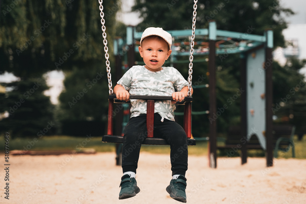 Swing children. Little boy having fun on a swing on the playground in public park. Happy child enjoy swinging. Active outdoors leisure for child in city. Swing children. Little boy having fun on a swing on the playground in public park. Happy child enjoy swinging. Active outdoors leisure for child in city.