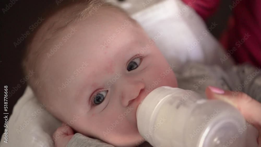 Mother feeding her baby son from milk bottle, holding him in hands, closeup detail Mother feeding her baby son from milk bottle, holding him in hands, closeup detail
