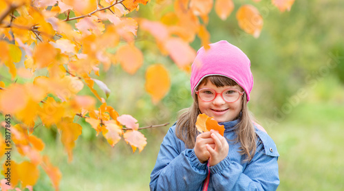 Smiling young girl with Downs syndrom holds autumn leaves. Empty space for text