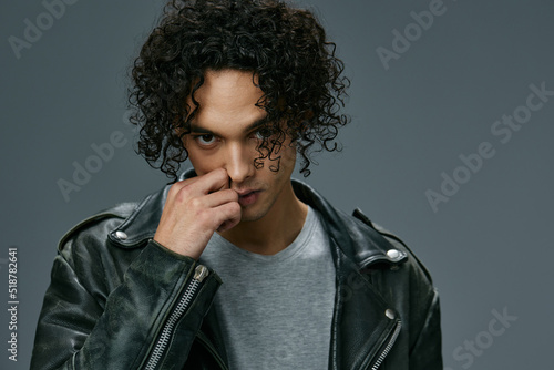 Sexy pretty stylish tanned curly man leather jacket looks at camera posing isolated on over gray studio background. Cool fashion offer. Huge Seasonal Sale New Collection concept. Copy space for ad