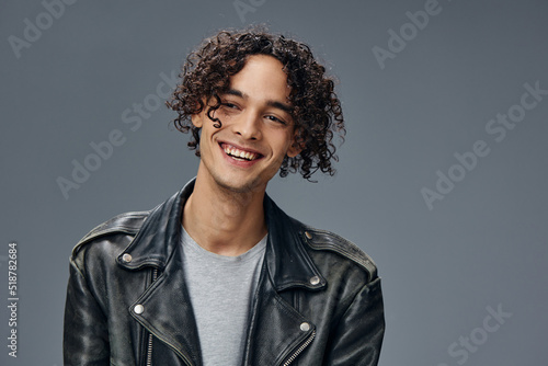Cheerful smiling stylish tanned curly man leather jacket posing isolated on over gray studio background. Cool fashion offer. Huge Seasonal Sale New Collection concept. Copy space for ad