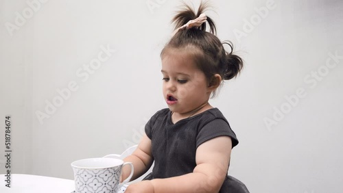 A little girl carries a mug after drinking tea. In the room.