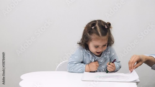 Cute little girl draws while sitting at the table at home. White background.