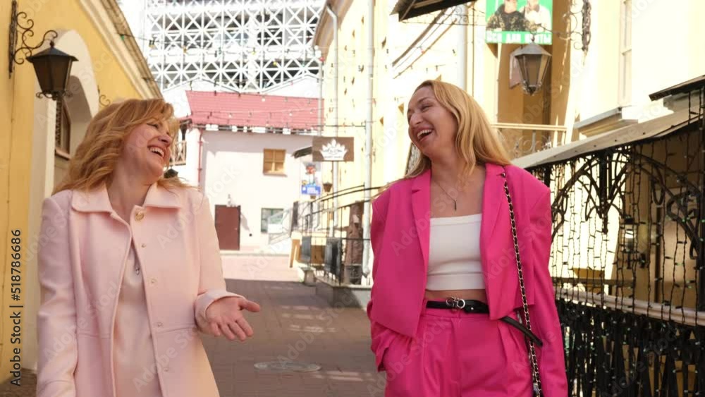 Two beautiful adult women girlfriends are walking along the city street and laughing. Slow motion video. Two beautiful adult women girlfriends are walking along the city street and laughing. Slow motion video.