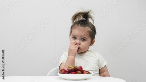 Cute little girl eats strawberries on a white background. Houses.