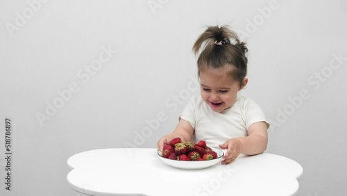 Funny little girl eats strawberries. On a white background.