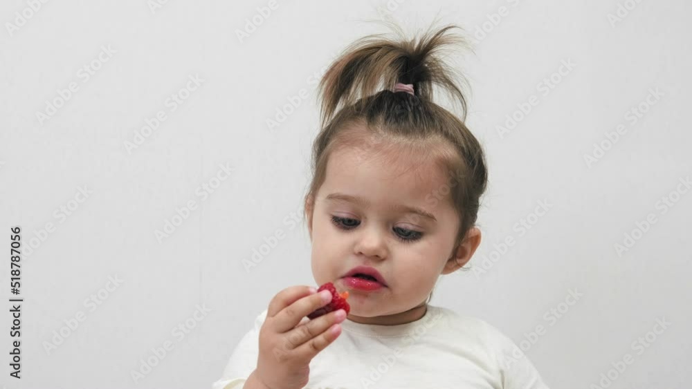 Cute little girl eats strawberries on a white background. Houses. Cute little girl eats strawberries on a white background. Houses.
