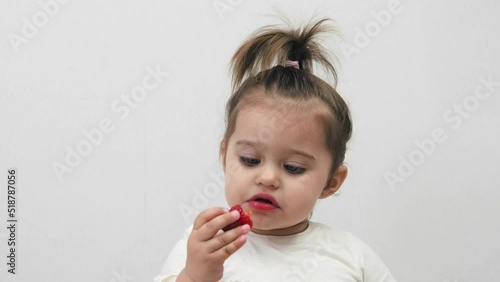 Cute little girl eats strawberries on a white background. Houses.