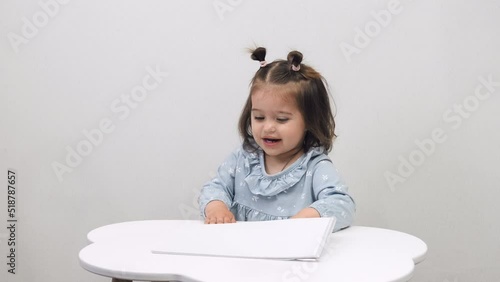 Cute little girl draws while sitting at the table at home. White background.