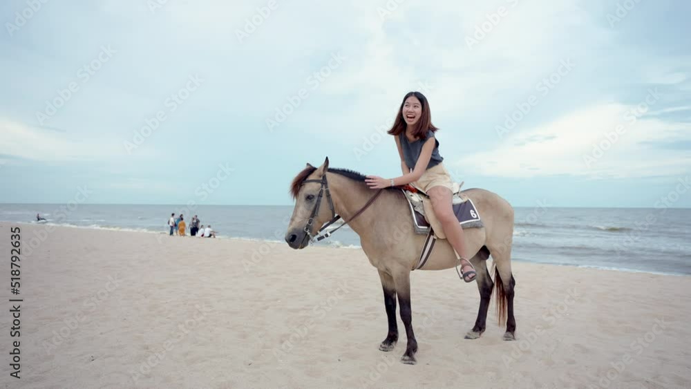 4K, A young Asian woman is walking happily on a horse on the sandy beach before the sun goes down. Tourists come to relax at the beach, ride horses, and take a walk. 4K, A young Asian woman is walking happily on a horse on the sandy beach before the sun goes down. Tourists come to relax at the beach, ride horses, and take a walk.