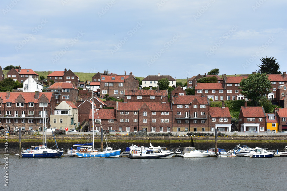 Obraz premium LANDSCAPE OF WHITBY ,THE SEASIDE TOWN OF NORTH YORKSHIRE.THE BRITISH HOUSES STYLE FROM BROWN BRICK WALL AND WHITE WINDOWS AND FISHING BOATS ,SPEED BOATS IN THE RIVER ERK