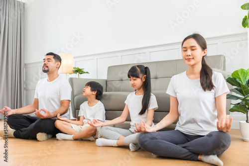 Lockdown  good for physical and mental health. Calm parents and children doing yoga at home. Happy Asian family with kids sitting and practicing meditation. © anon