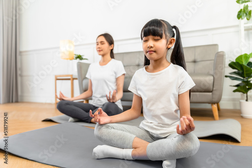 Asian young mother and her daughter setting prepare to yoga and meditation pose together on yoga mat in living room at home. Fitness lifestyle.