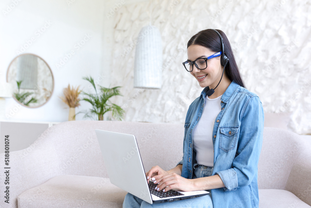 Young beautiful woman working at home sitting on sofa, using headset and laptop for video call, tech support of online store, and customer service worker Young beautiful woman working at home sitting on sofa, using headset and laptop for video call, tech support of online store, and customer service worker