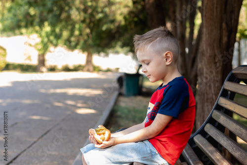 cute boy holding a hot dog in his hands while sitting on a park bench