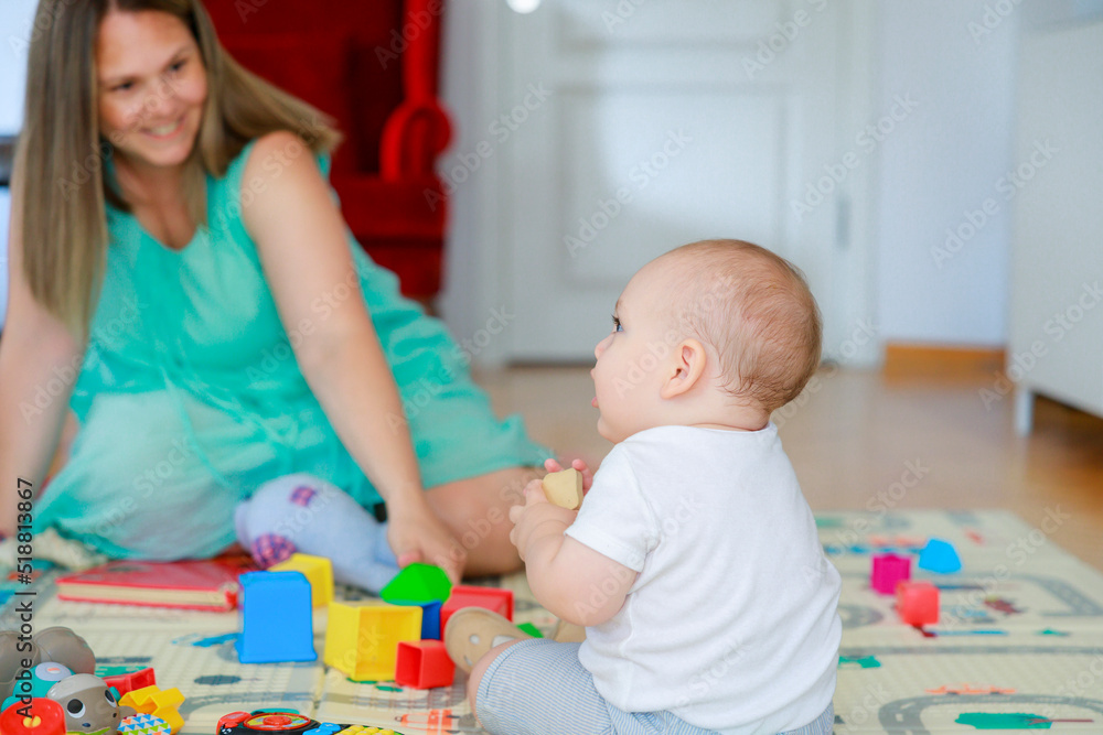 Baby boy and his mother sitting on the floor, having fun with toys