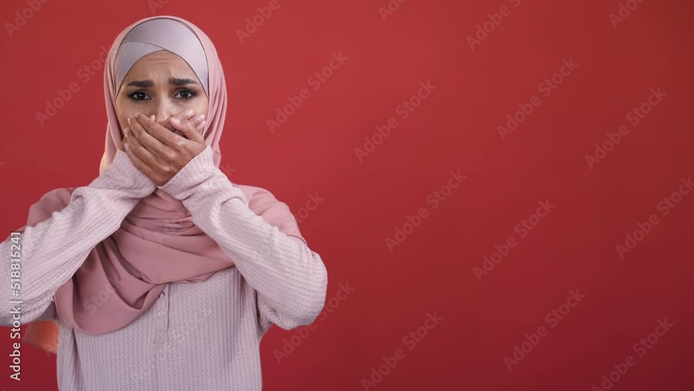 Female rights. Woman discrimination. Gender equality. Upset scared speechless lady in hijab covering mouth with hand isolated on red empty space background. Female rights. Woman discrimination. Gender equality. Upset scared speechless lady in hijab covering mouth with hand isolated on red empty space background.
