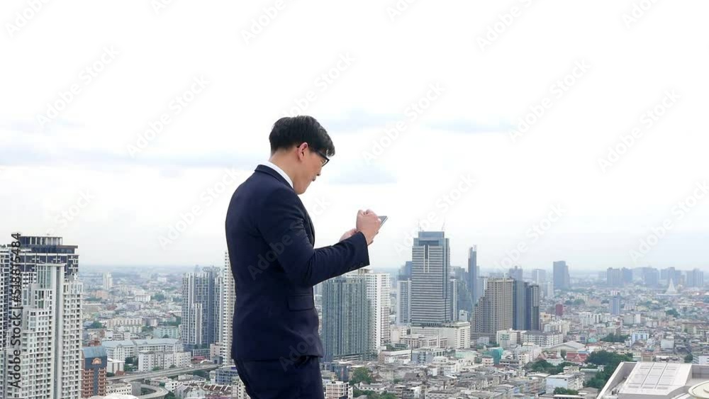 Video of Asian businessman in dark blue suit, wearing glasses standing on rooftop of building Lifted his hand and shouted, happy to succeed in work, successful business with Cityscape background. Video of Asian businessman in dark blue suit, wearing glasses standing on rooftop of building Lifted his hand and shouted, happy to succeed in work, successful business with Cityscape background.