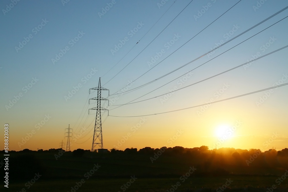 Silueta de torres de alta tensión para la conducción de electricidad. Imagen tomada al atardecer con los últimos rayos del sol al ponerse este en el horizonte. Madrid, España.