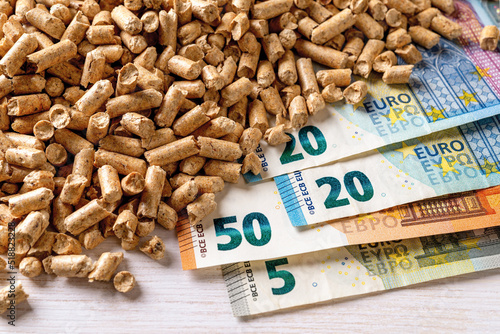 Heap of wood pellets and euro paper banknotes top view. Costs of organic biofuel from compressed sawdust. Ecological heating, alternative energy concepts. Bio fuel costs, buy and sell pellets. photo