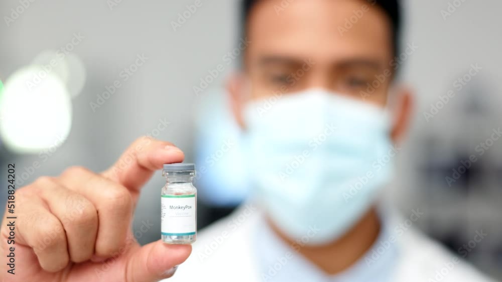 Hand of doctor holding a vaccine for a virus or covid inside against a blurred background. Closeup portrait of a medical researcher wearing a mask and showing a glass vile with flu injection at a lab Hand of doctor holding a vaccine for a virus or covid inside against a blurred background. Closeup portrait of a medical researcher wearing a mask and showing a glass vile with flu injection at a lab