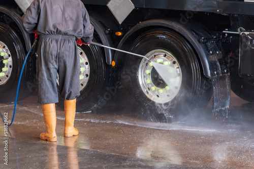 Operator of a truck wash cleaning the tires with pressurized water. photo
