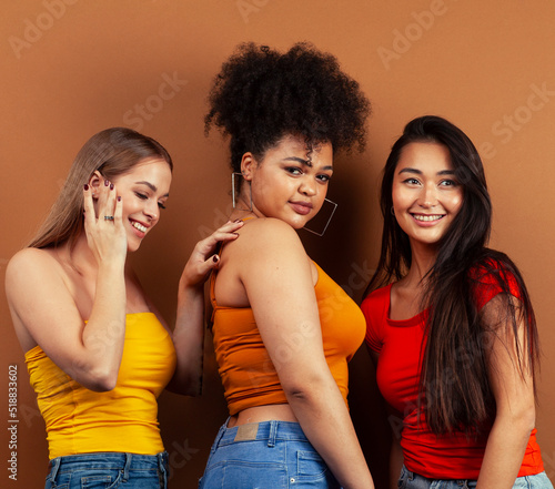 young pretty african and caucasian women posing cheerful together on brown background, lifestyle diverse nationality people concept