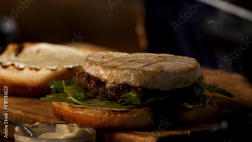 Close up of male hands putting camembert cheese on homemade hamburger with sauce and greenery, foodporn concept. Stock footage. Preparation of fat tasty burger.